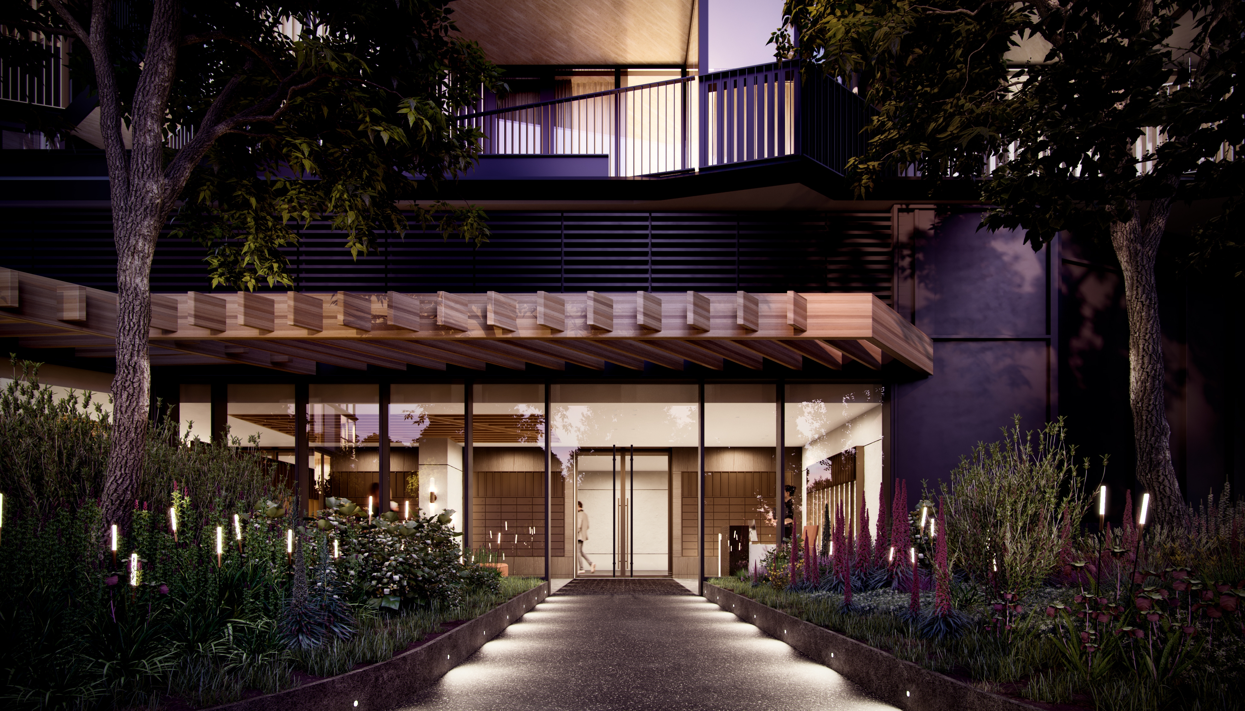 Foto van de verlichte ingang met een verlicht pad en bomen aan de linker en rechterkant 